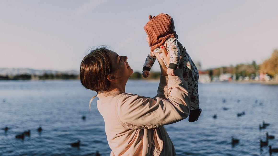 Une mère tient son bébé en l’air en face d’un lac