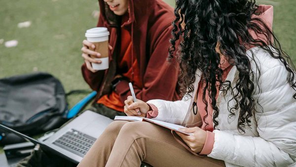 Coûts pour les frais de scolarité et autres dépenses. Deux étudiantes assises sur l’herbe étudient ensemble