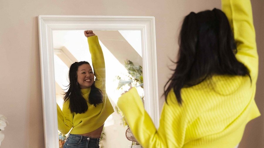 Une femme en pull jaune étire ses bras devant le miroir