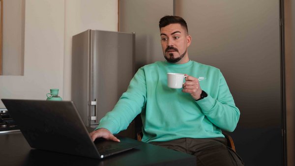 Un homme choqué est assis devant un ordinateur portable avec un verre dans la main