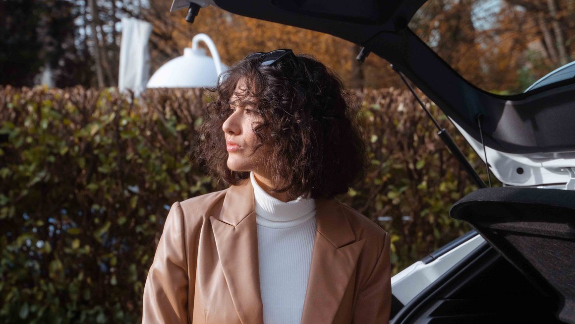 Une jeune femme se tient debout devant le coffre ouvert de sa voiture