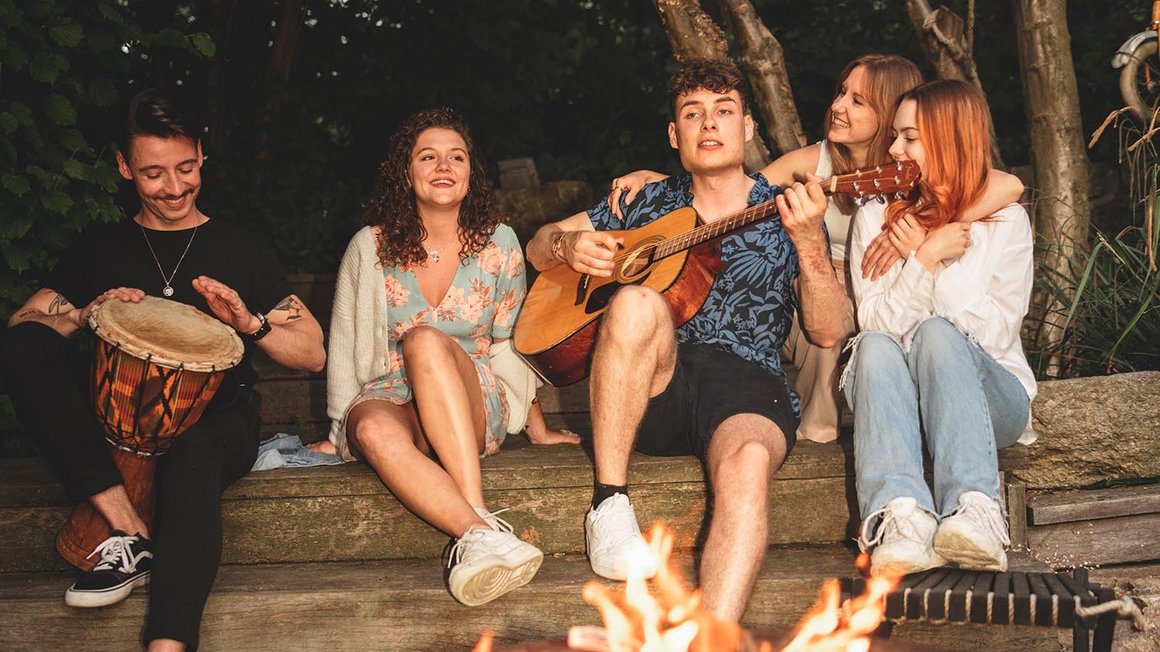 Quatre amis assis autour d’un feu jouent de la guitare
