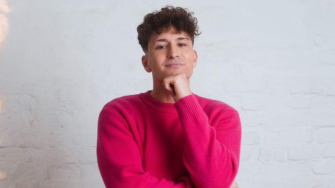 La sécurité avant tout : réduction des dettes et constitution d'une épargne de précaution Un homme dans un pull rose regarde l’appareil photo de façon pensive