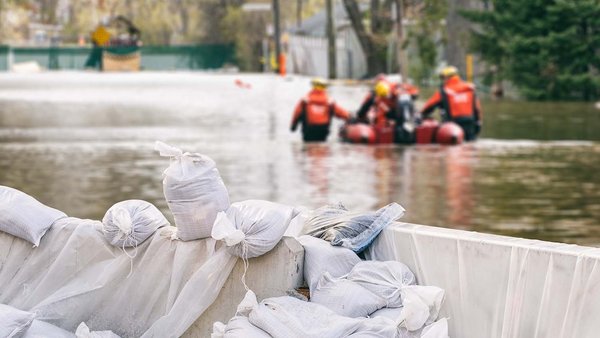 Des maisons inondées protégées par des sacs de sable et une équipe de secours en arrière-plan