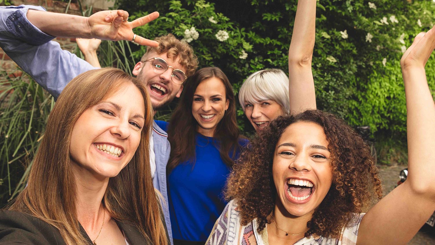 Planifier des vacances entre amis : comment ça marche ? Cinq amis tout sourire riant ensemble face à un appareil photo