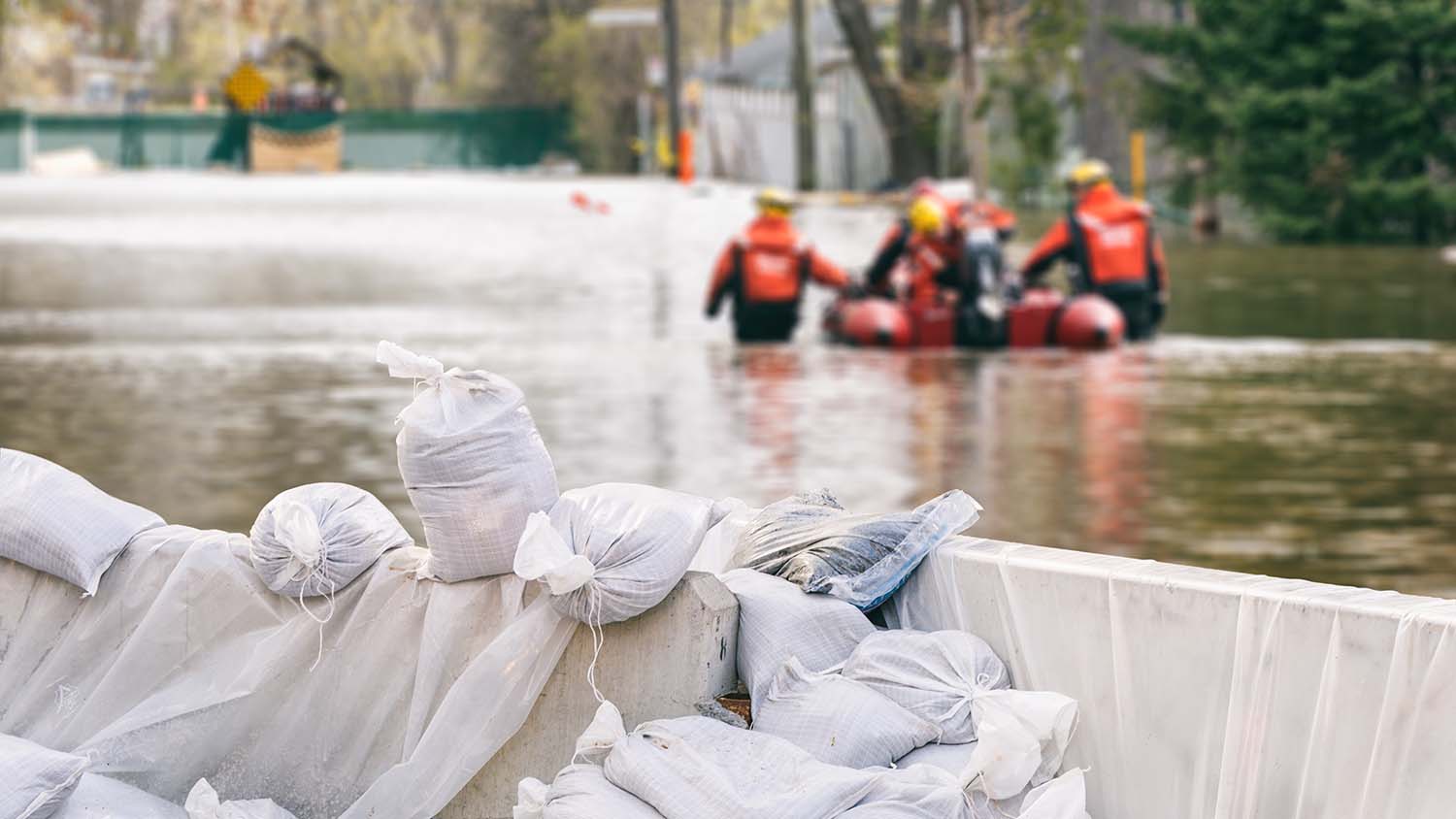 Des maisons inondées protégées par des sacs de sable et une équipe de secours en arrière-plan