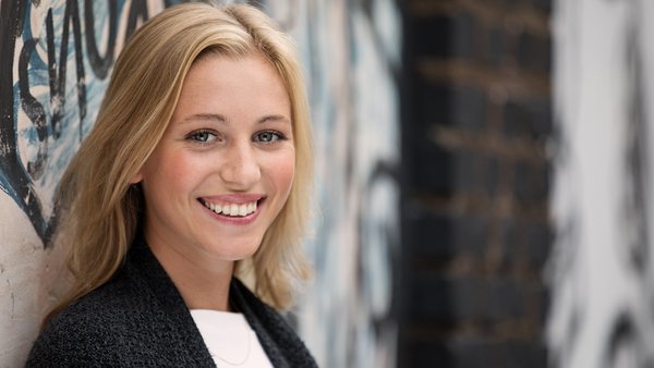 Une femme blonde regarde devant elle en souriant.