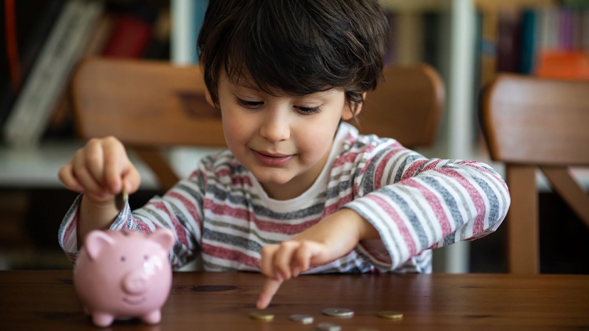 Un enfant avec une tirelire et des pièces de monnaie – frais fixes mensuels dans le foyer