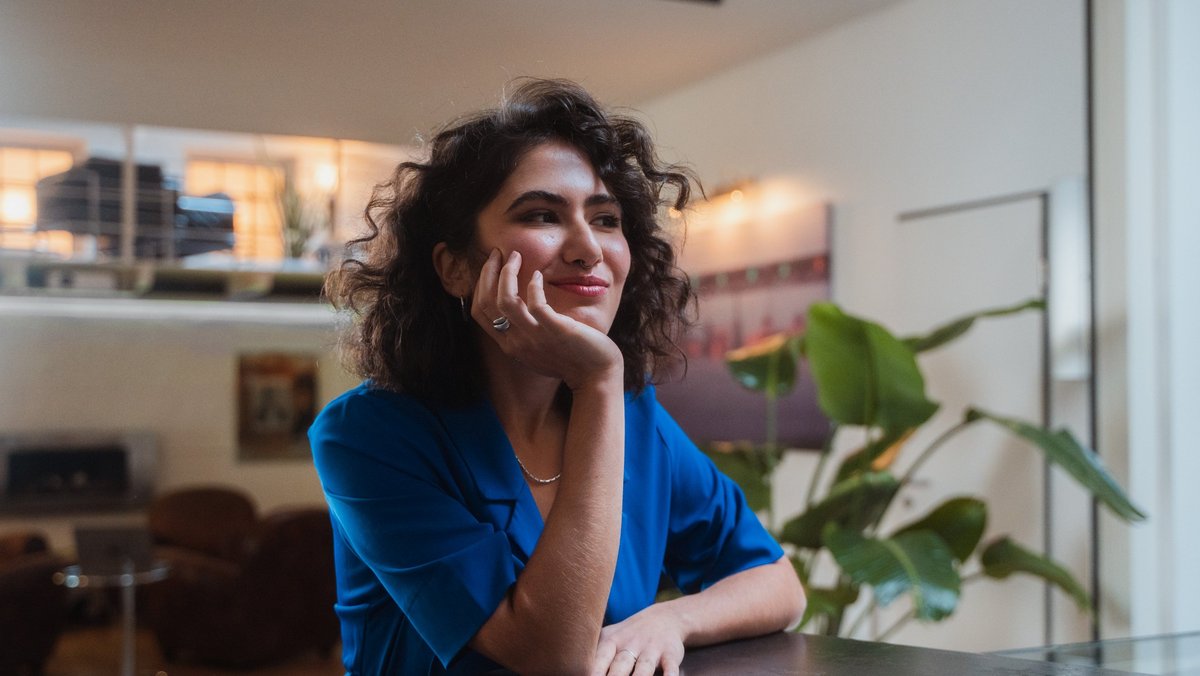 Une jeune femme en chemisier bleu regarde gentiment sur le côté.
