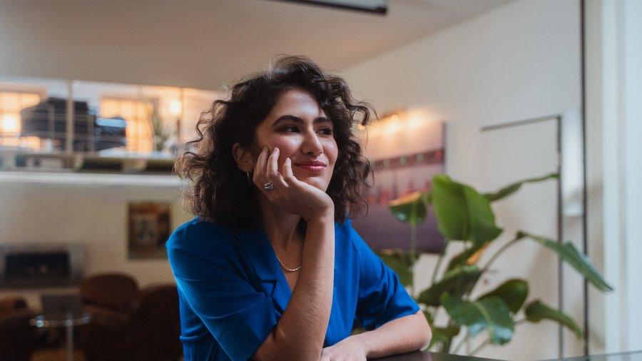 Jeune femme aux boucles brunes regardant sur le côté en souriant.