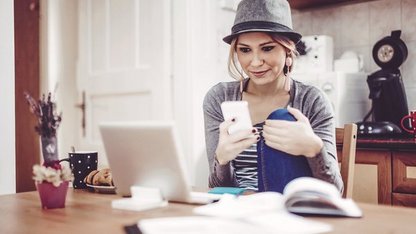 Jeune femme à table avec un smartphone, un cahier et des documents qui fait les comptes de son foyer