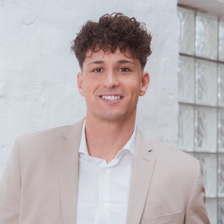 Un jeune homme en costume gris sourit aimablement à la caméra.