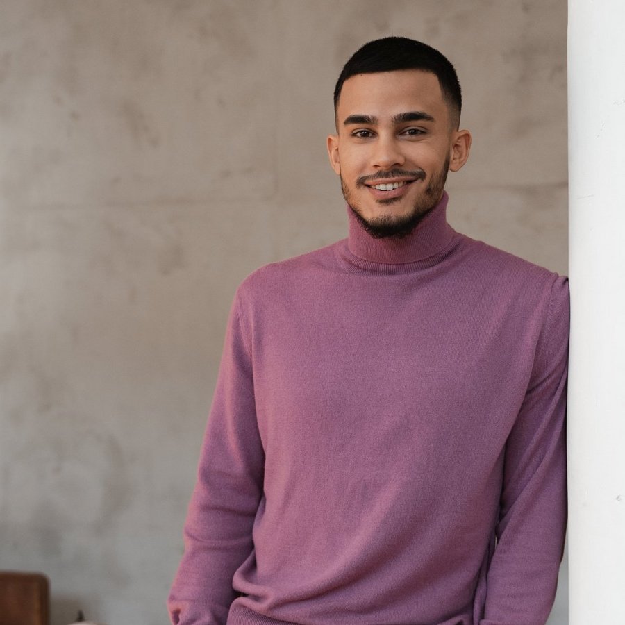 Un jeune homme aux cheveux courts et foncés regarde la caméra en souriant chaleureusement.